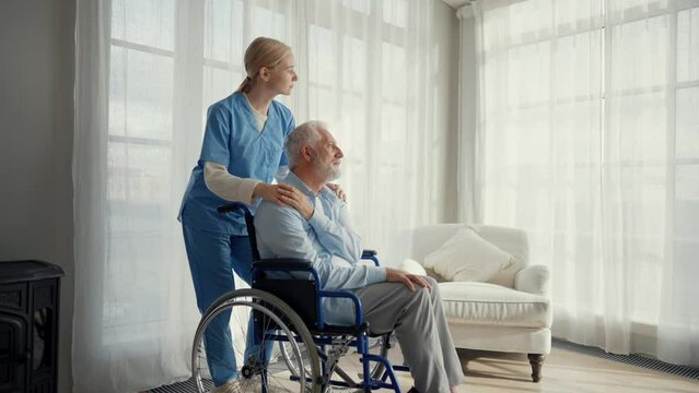 Nurse massaging neck to paralyzed man. Senior male in wheelchair enjoying massage at clinic. Medical worker provides care support help. Living with legs paralysis, special needs people concept.