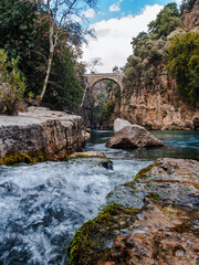 Fototapeta na wymiar Bottom view of the ancient arched bridge across the Koprucay River gorge in Koprulu National Park in Turkey. A beautiful mountain turquoise river with a fast flow, green bushes clinging to the rocks.