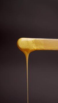 yellow golden liquid wax sugar paste for depilation drops from the wooden spatula black background close-up