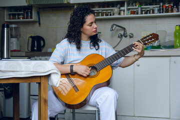 young latin woman practicing acoustic guitar at home