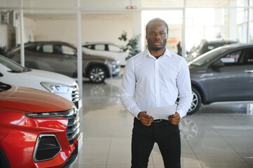 Portrait Of Handsome African American Salesman At Workplace In Car Showroom