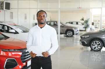 Cars Dealership Concept. Auto Seller Afro Man Standing In Automobile Center