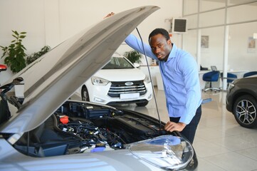 handsome african businessman is examining a car before buying it, he checks all characteristics and...