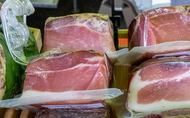Speck - smoked pork meat wrapped in transparent plasticon sale at the Italian food market. Italy - 718800899