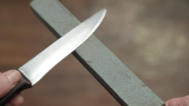 Sharpening knife blade using hand sanding tool. Shallow depth of field.