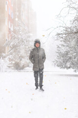 A boy walks along a snowy street, it is snowing, blizzard and frost on a winter day