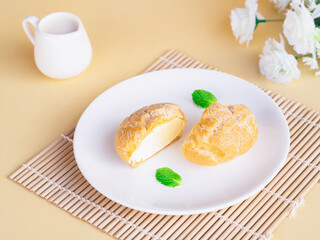 Half cut soft choux cream puff custard flavor in white plate on beige background. Baked Goods style and Minimalist product concept