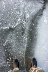 Walking on thin ice with a crack. View of feet that stand on the ice of a frozen pond in winter