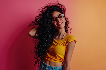 Cheerful young woman with long curly hair and stylish glasses, wearing a bright yellow top, exudes confidence against a gradient pink background.