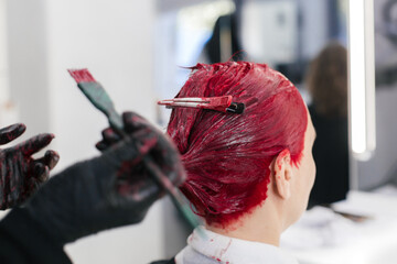 master hairdresser colorist dyes the roots of a woman with red hair