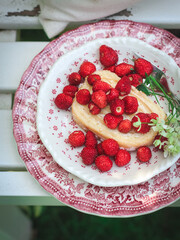 Wild strawberries on a slice of cake served on a white bench, shot from above