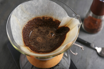 Glass chemex coffeemaker with paper filter and coffee on table, closeup