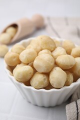 Tasty peeled Macadamia nuts in bowl on white table, closeup