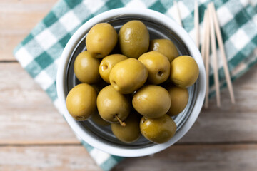 Green olives in a bowl on wooden table. Top view