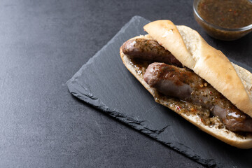 Traditional choripan, Argentina sandwich with chorizo and chimichurri sauce on black slate background