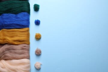 Colorful felting wool and balls on light blue background, flat lay. Space for text