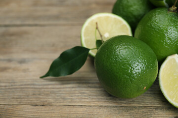 Fresh limes and leaves on wooden table, closeup. Space for text