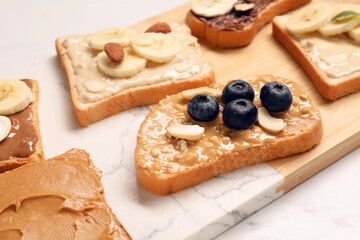 Toasts with different nut butters, fruits and nuts on white table, closeup