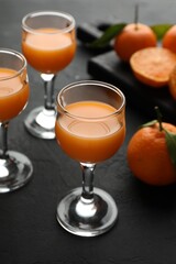 Tasty tangerine liqueur in glasses and fresh citrus fruits on black textured table