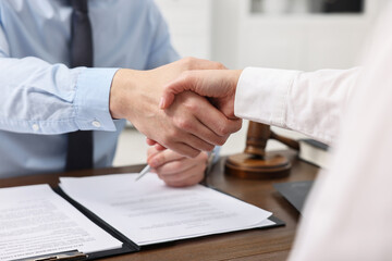 Lawyers shaking hands at wooden table in office, closeup