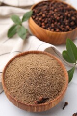 Aromatic clove powder and dried buds in bowl on white table, closeup