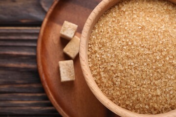 Brown sugar in bowl and cubes on wooden table, top view