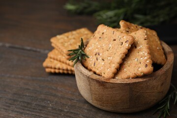 Cereal crackers with flax, sesame seeds and rosemary in bowl on wooden table, closeup. Space for text