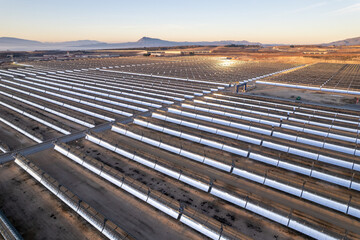 Solar thermal power plant at sunrise. Mirrors reflecting the sun, heating the water flowing through a metallic tube passing through a turbine that converts steam into electricity. Aerial photo