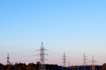 Electric line masts in a wooded area against a blue sky background