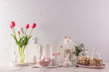 Fototapeta na wymiar Chic kitchen background in delicate pastel colors, decorated for the Easter holiday with rabbits, flowers, eggs. White cookware.