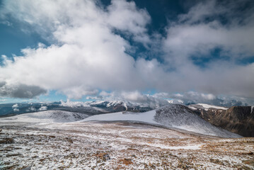 Vast colorful alpine view to snowy stony pass and large snow-white mountain range in far away among low clouds. Most beautiful rocky hill in freshly fallen snow among high mountains under cloudy sky.