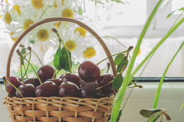 Close-up of ripe cherries in a small basket on a window with a blurred background. Selective focus, daylight