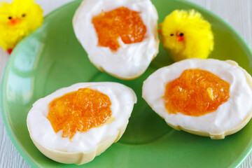 homemade white chocolate half easter eggs stuffed with cream cheese and orange jam looks like white and yolk. On green plate with chick close up. Easter egg with pudding cream, Easter dessert concept