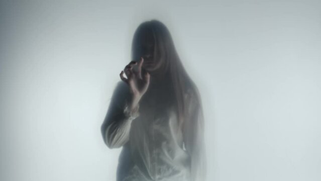 Melancholic female silhouette behind a transparent frosted curtain or glass close up. A seminude man approaches the woman from behind, turns her towards him and they embrace.