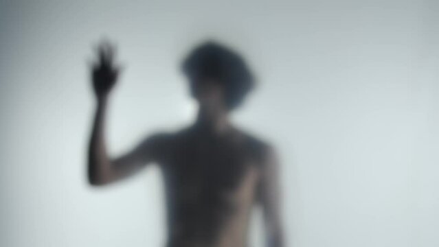 Male silhouette behind a transparent frosted curtain or glass close up. A man is guiding her hand on the surface of the curtain.