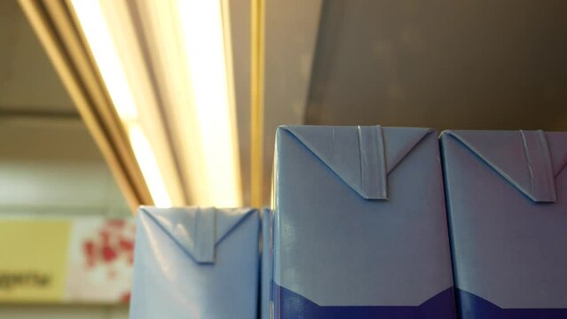Close-up of milk cartons on a supermarket shelf and a buyer's hand takes one