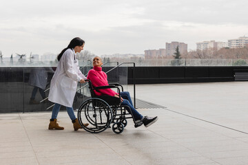 female doctor pushes bald cancer patient in wheelchair to clear her head and takes a breath