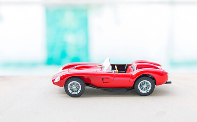 Red sport model car on swimming pool edge with space on blurred background, outdoor day light
