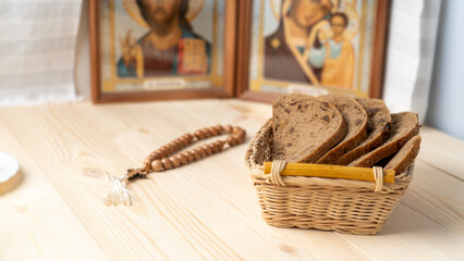 Bread in a wicker basket, rosaries and icons on a wooden table during the great Christian Lent,...