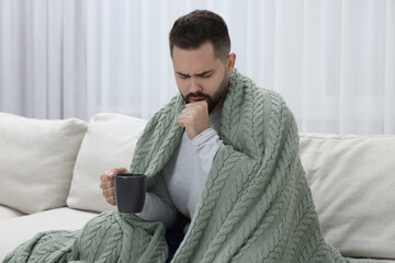 Sick man with cup coughing at home