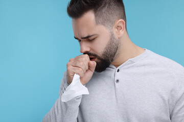 Sick man with tissue coughing on light blue background, space for text
