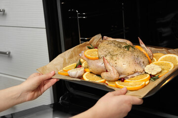 Woman putting chicken with orange slices into oven, closeup