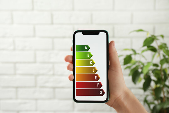Energy efficiency. Woman using smartphone with colorful rating on display indoors, closeup