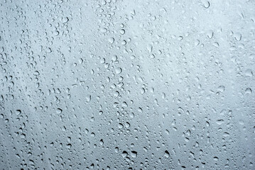 Closeup of rain drops on window on grey sky background
