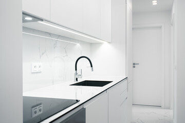 A Modern, bright kitchen with white cabinets, marble countertops, and a sleek sink under minimalist...
