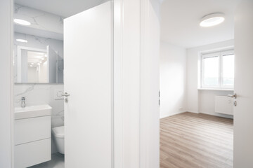 modern, bright interior with a bathroom featuring white fixtures and marble walls, adjacent to an empty room with wooden flooring.