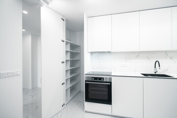 A Modern, white kitchen with sleek cabinets, a built-in oven, and a contrasting black countertop line. Marble-like walls add elegance.