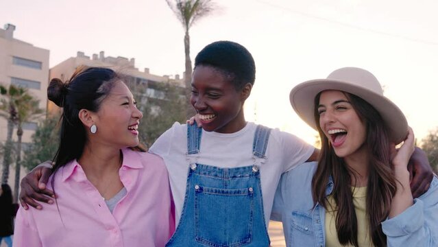 Group multiracial young friends walking embracing looking smiling at camera enjoying summer vacation excited together outdoor. Three pretty women of generation z strolling happy hugging on sunny day