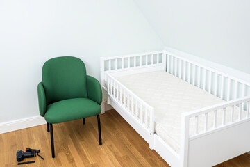 A simple nursery room featuring a white crib and a green chair against a plain background, suggesting a clean and modern aesthetic.