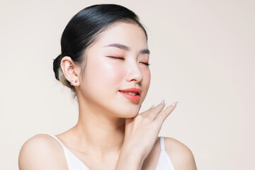 Young gorgeous asian woman touches her jaw line on beige background.